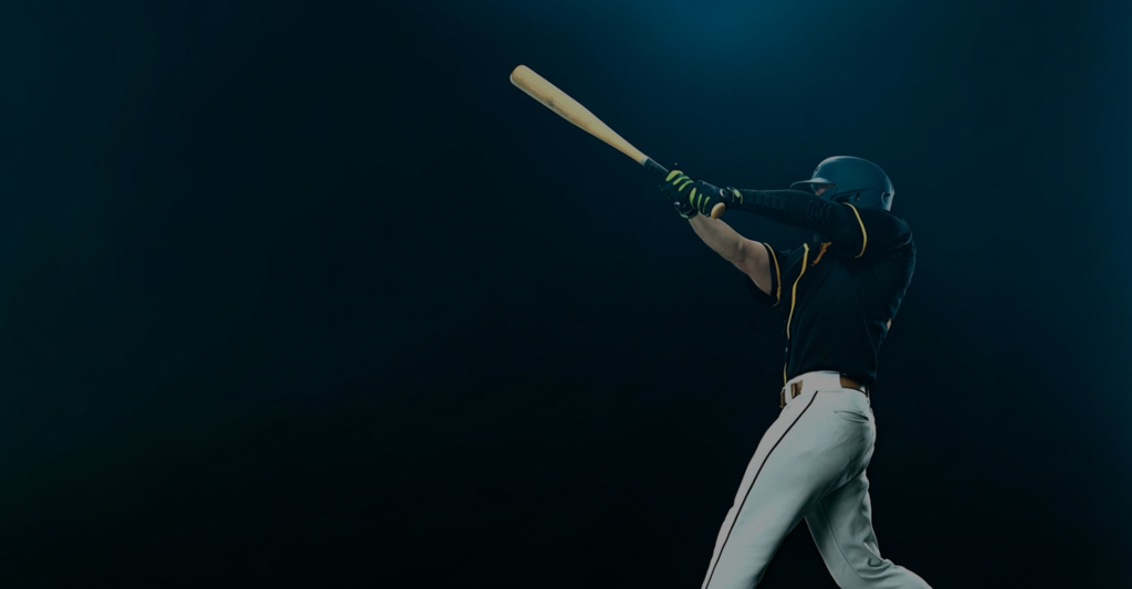 Baseball player swinging bat against dark background